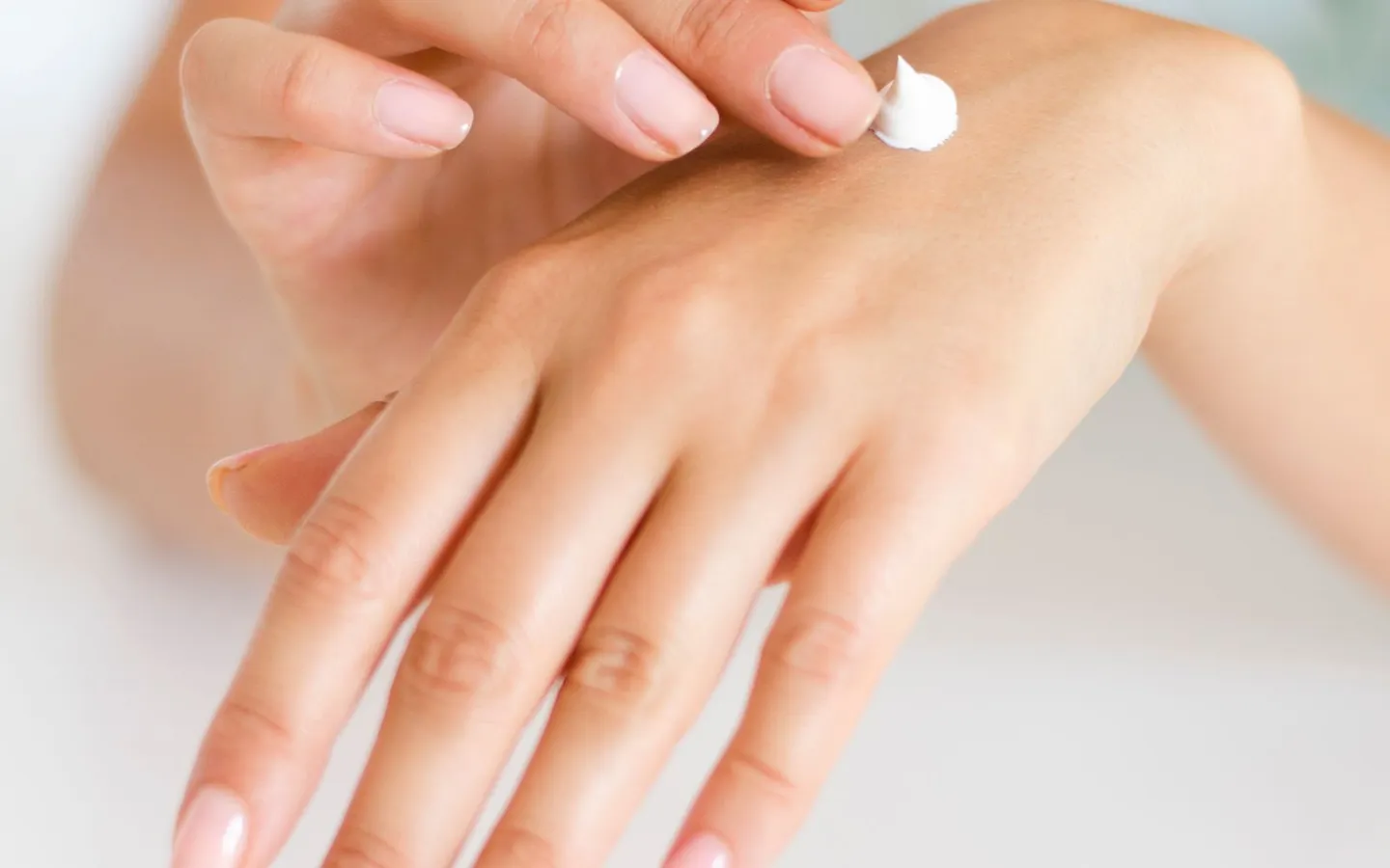 A person applying moisturizing cream to the back of their hand