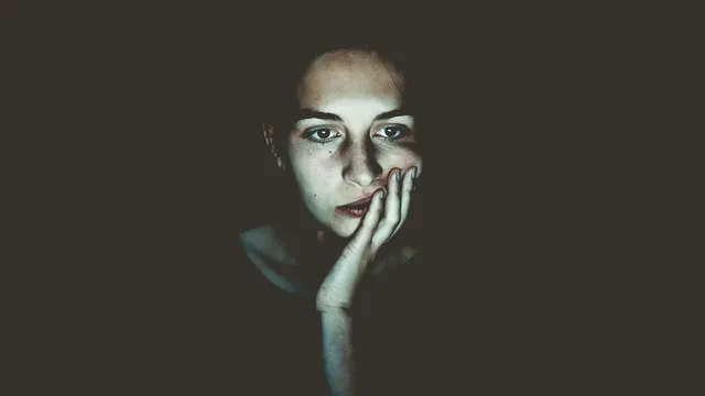 Person resting their head on their hand, looking thoughtful in low light
