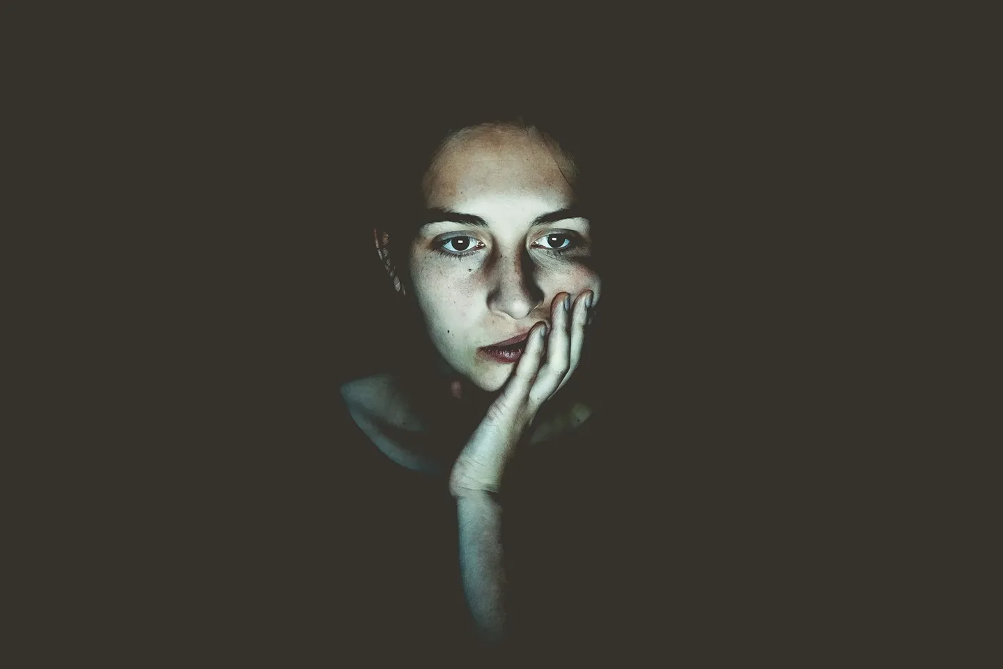 Person resting their head on their hand, looking thoughtful in low light