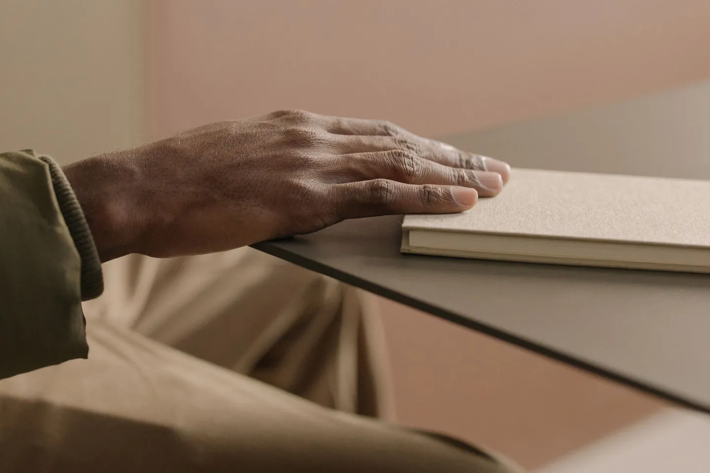 Close-up of a hand resting calmly on a beige notebook on a table