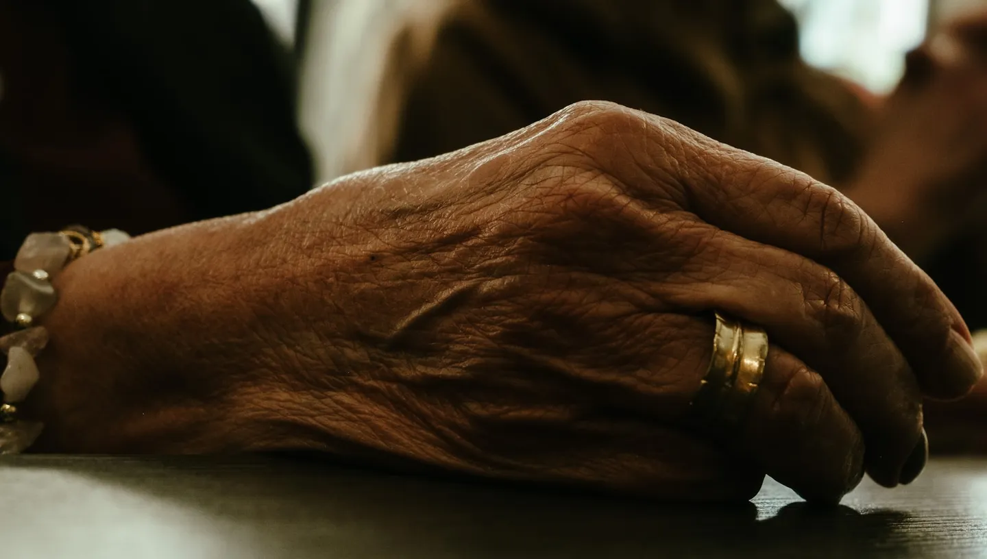 A person's hand resting on a wooden table in warm afternoon light