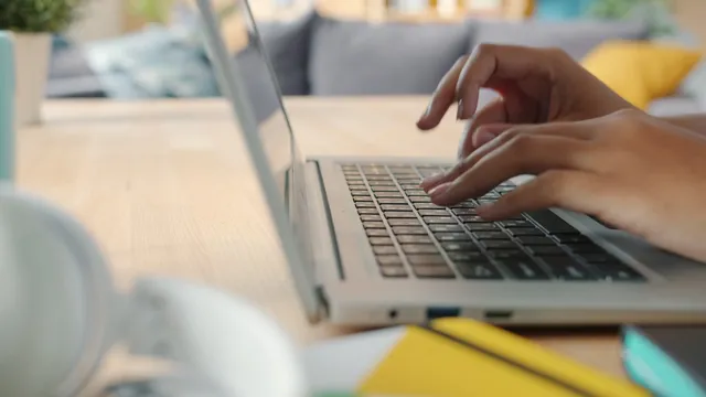 A person's hands typing on a laptop keyboard at a home desk