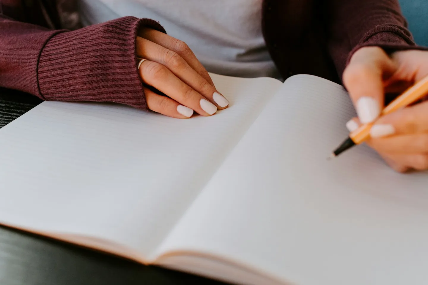 A person's hands writing in a blank notebook at a calm, neutral desk