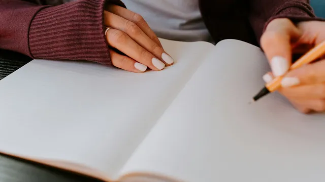 A person's hands writing in a blank notebook at a calm, neutral desk